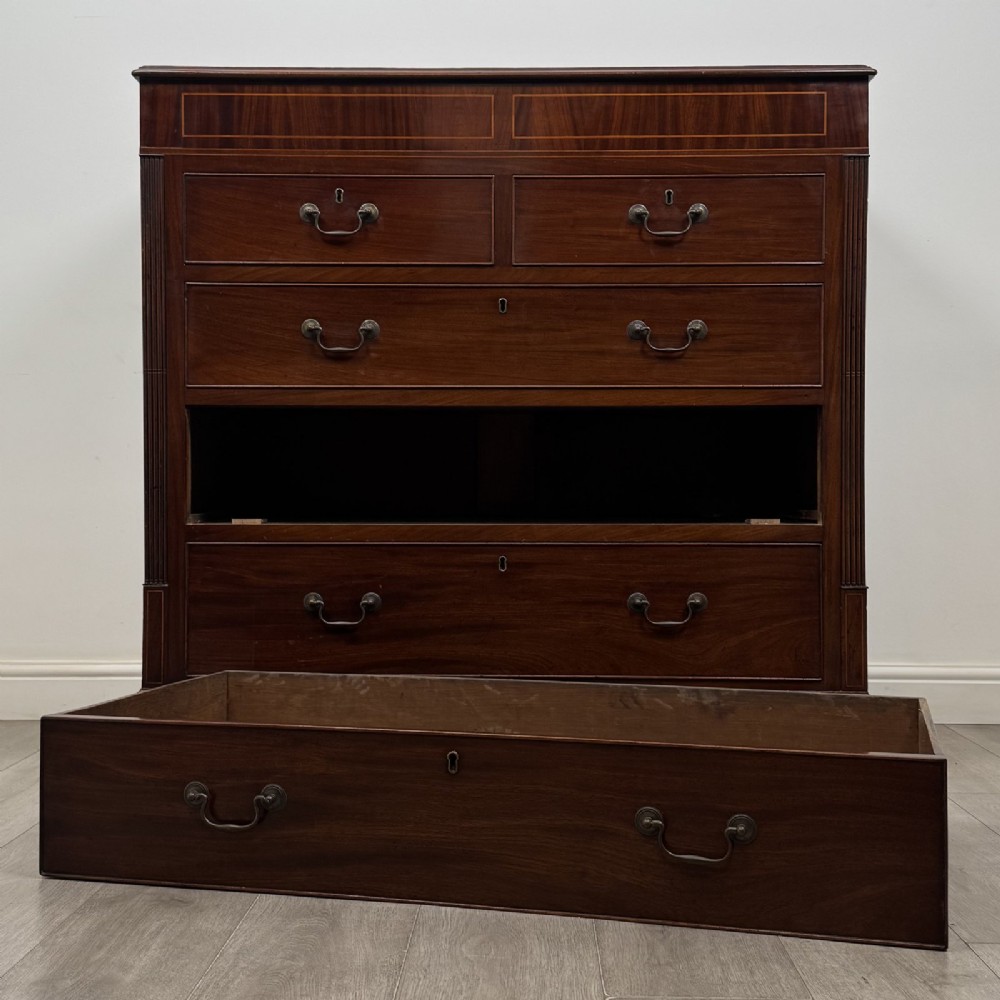 An 18th-century Georgian mahogany chest of drawers featuring inlaid stringing along the top frieze, two short drawers above three long drawers, brass swan-neck handles, fluted pilasters, and bracket feet. View X