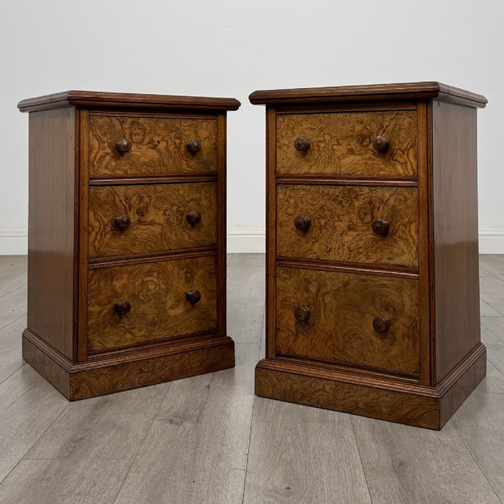 A pair of Victorian burr walnut bedside cabinets featuring three drawers each with turned wooden knobs and a plinth base.