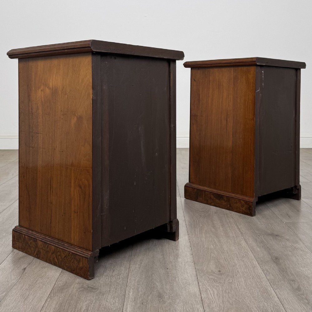 A pair of Victorian burr walnut bedside cabinets featuring three drawers each with turned wooden knobs and a plinth base. View V