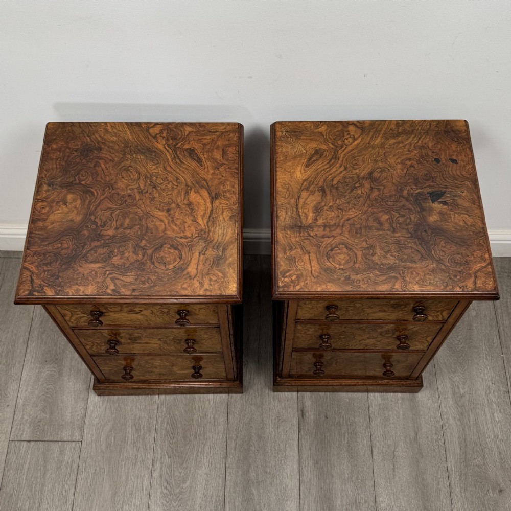 A pair of Victorian burr walnut bedside cabinets featuring three drawers each with turned wooden knobs and a plinth base. View X