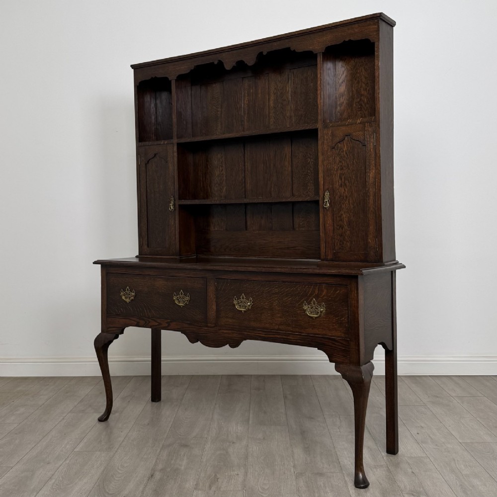 A dark oak Queen Anne style dresser featuring an open-shelf upper rack with side cupboards above two drawers supported by cabriole legs. View II