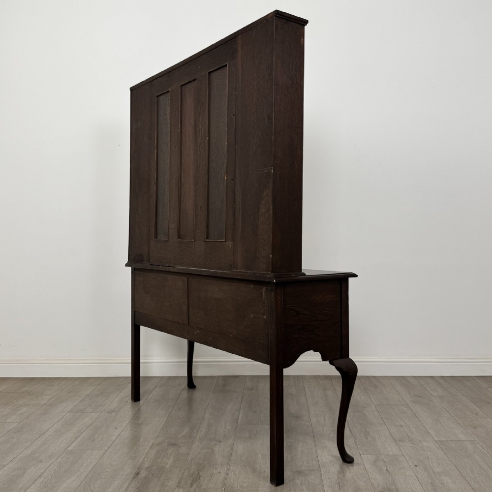 A dark oak Queen Anne style dresser featuring an open-shelf upper rack with side cupboards above two drawers supported by cabriole legs. View VI
