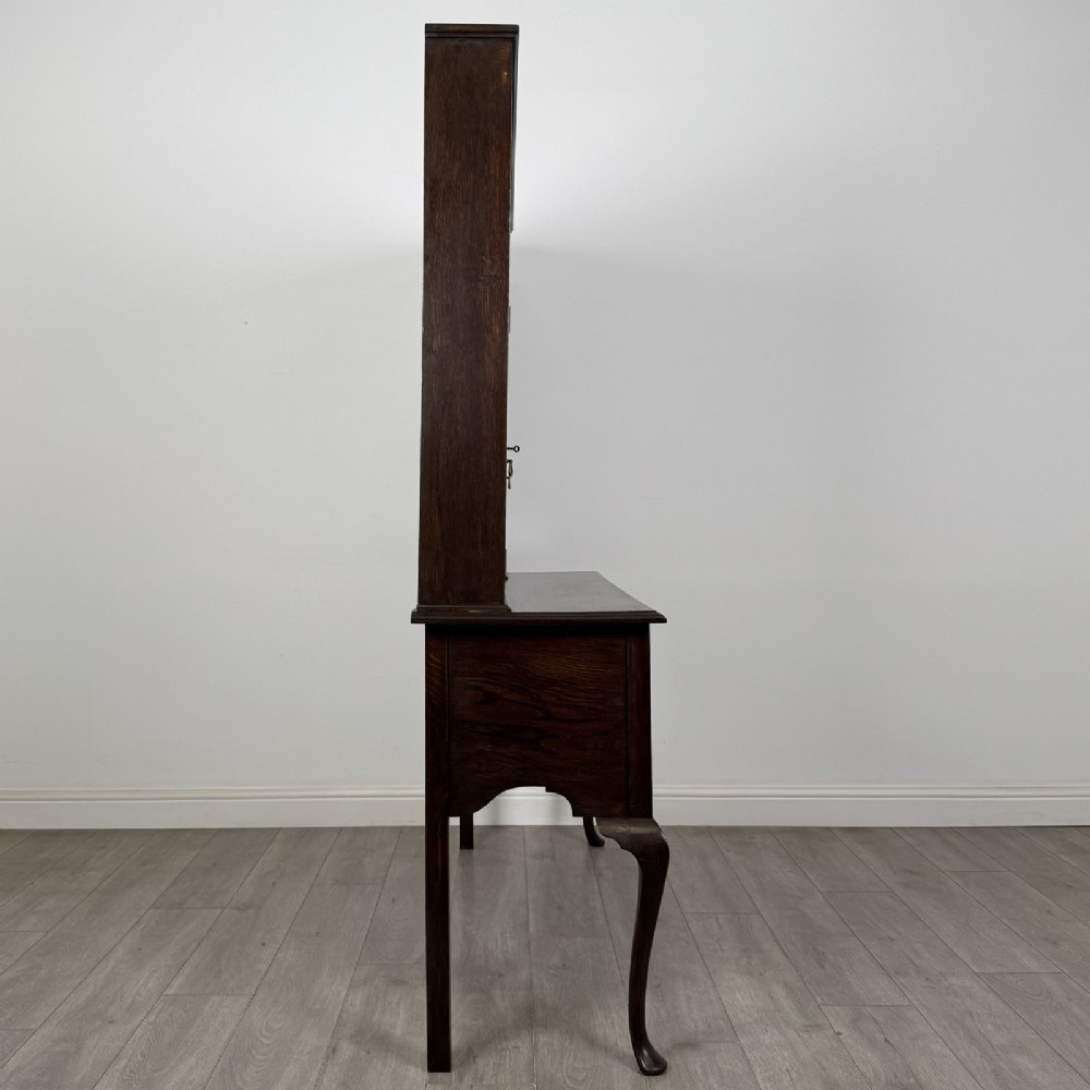 A dark oak Queen Anne style dresser featuring an open-shelf upper rack with side cupboards above two drawers supported by cabriole legs. View VII