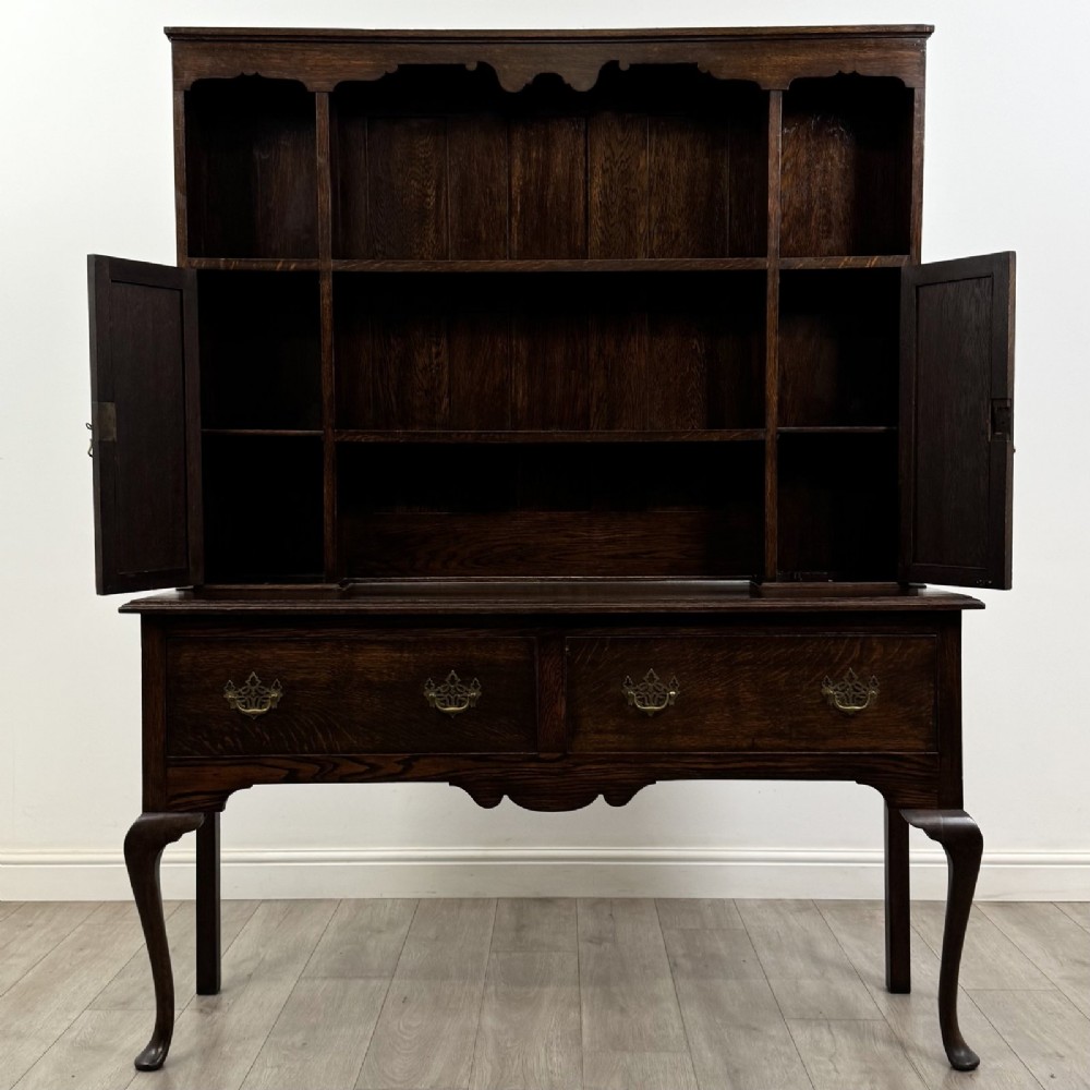 A dark oak Queen Anne style dresser featuring an open-shelf upper rack with side cupboards above two drawers supported by cabriole legs. View IX