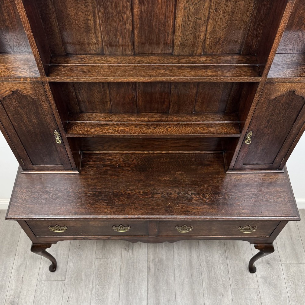 A dark oak Queen Anne style dresser featuring an open-shelf upper rack with side cupboards above two drawers supported by cabriole legs. View X
