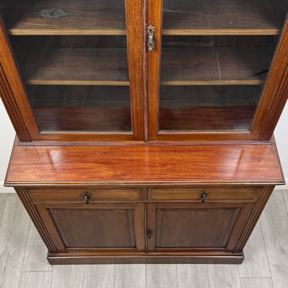 An antique Victorian mahogany glazed bookcase featuring two upper glass doors, twin frieze drawers, and lower panelled doors. View XI