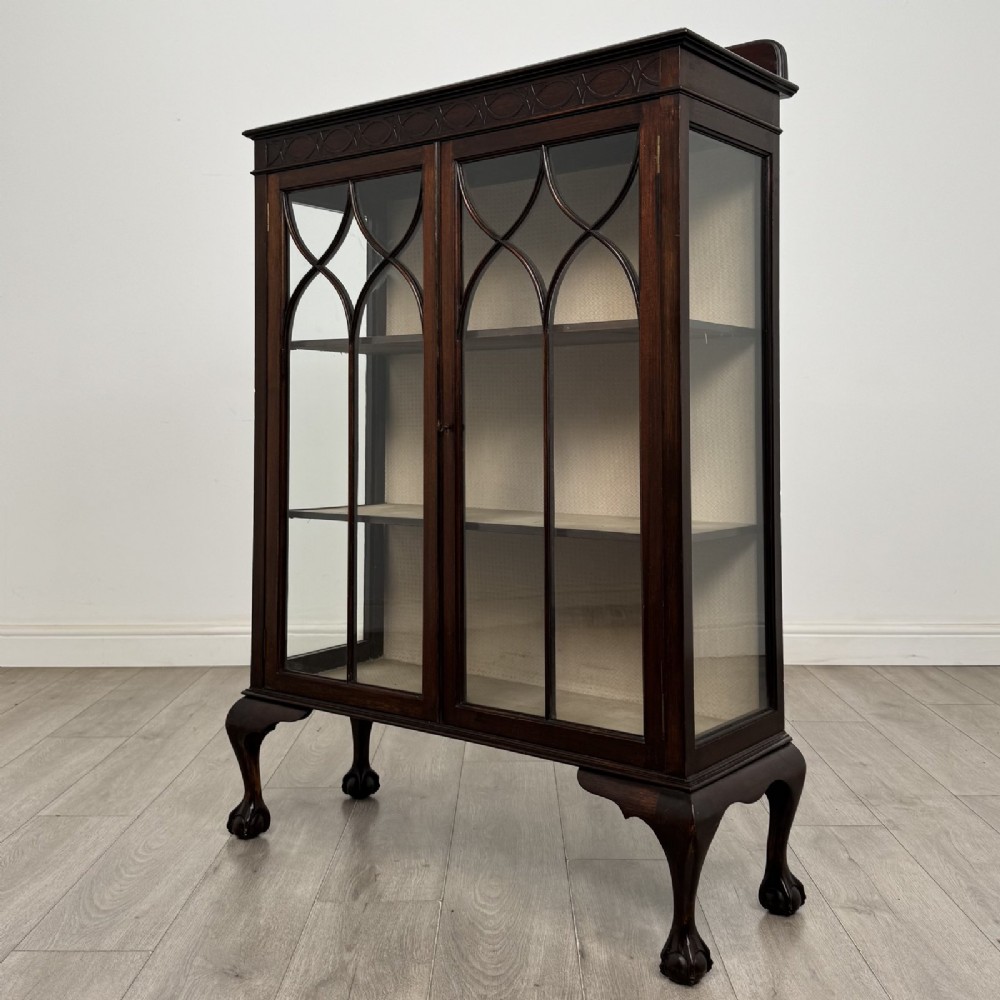 A dark mahogany display cabinet featuring two glazed doors with geometric arch bars and carved ball-and-claw feet. View II