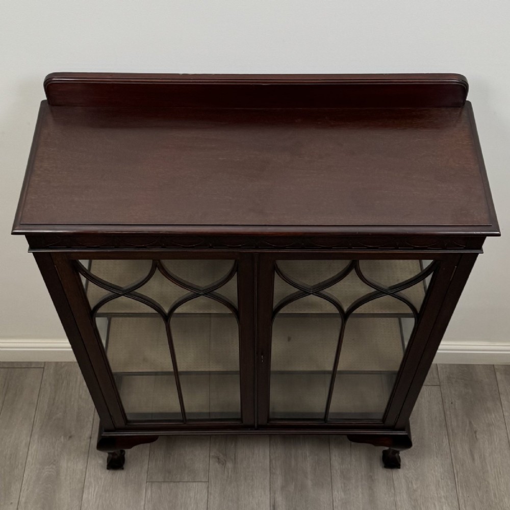 A dark mahogany display cabinet featuring two glazed doors with geometric arch bars and carved ball-and-claw feet. View X