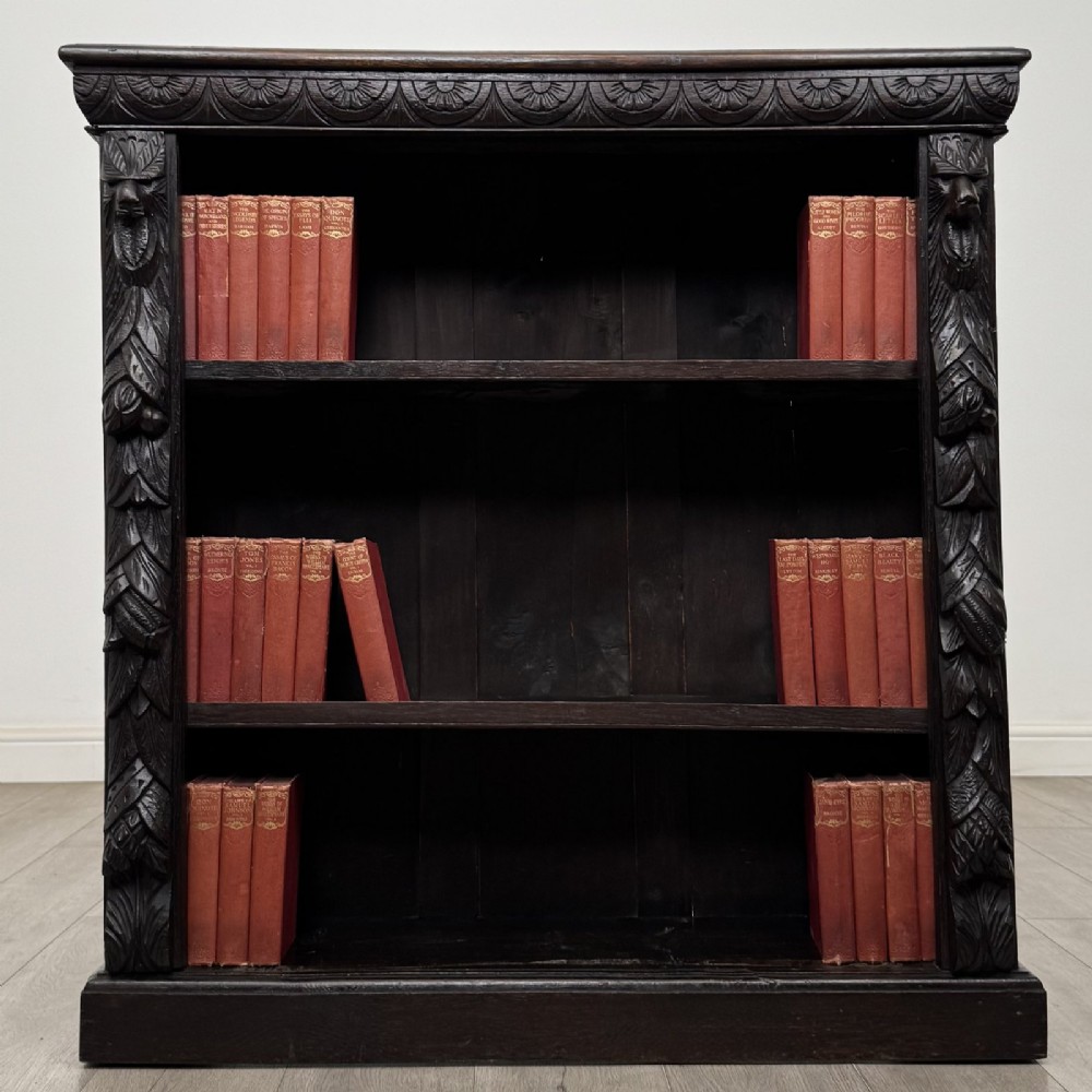 A dark carved oak open bookcase featuring three shelf surfaces and pilasters detailed with foliate carvings and Green Man masks. View II