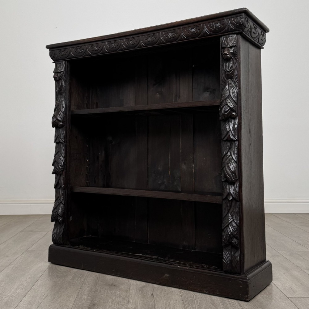A dark carved oak open bookcase featuring three shelf surfaces and pilasters detailed with foliate carvings and Green Man masks. View III