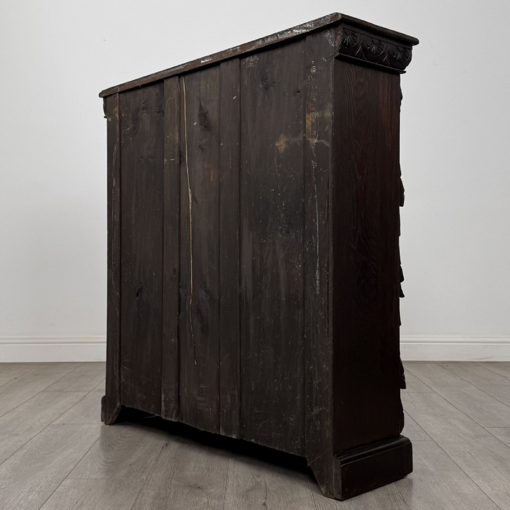 A dark carved oak open bookcase featuring three shelf surfaces and pilasters detailed with foliate carvings and Green Man masks. View VII