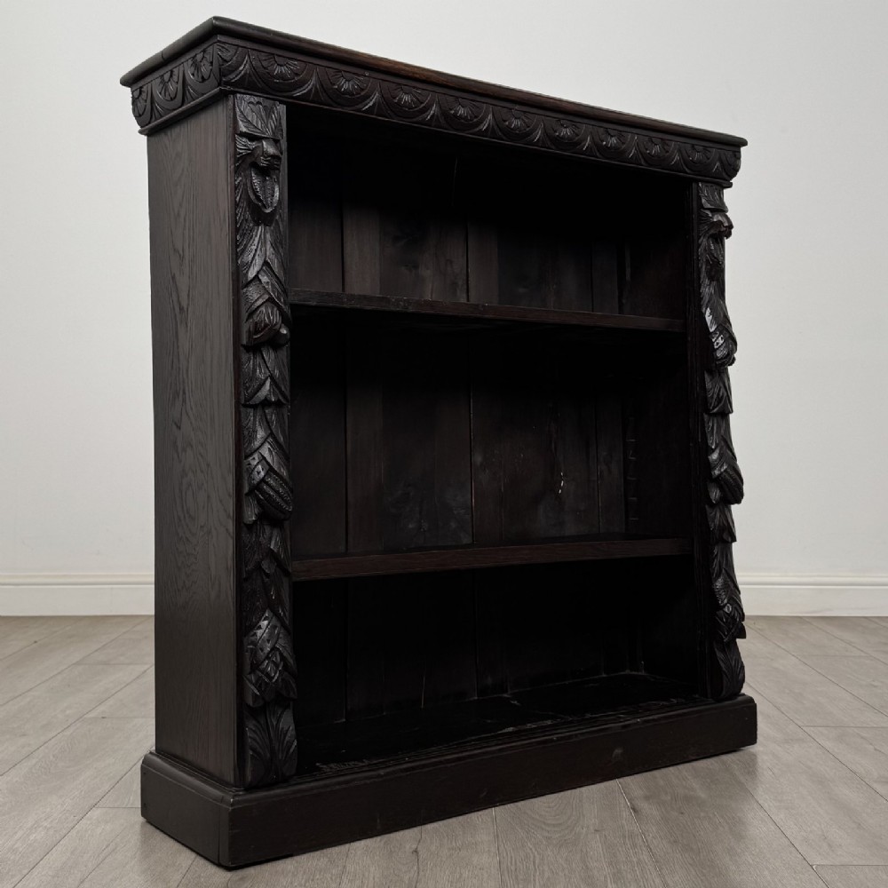 A dark carved oak open bookcase featuring three shelf surfaces and pilasters detailed with foliate carvings and Green Man masks. View IX