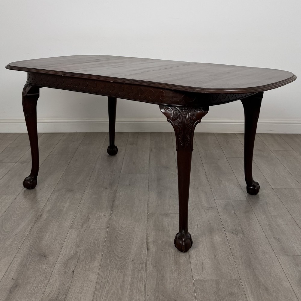 An Edwardian mahogany extending dining table featuring a carved frieze and cabriole legs terminating in ball-and-claw feet.
