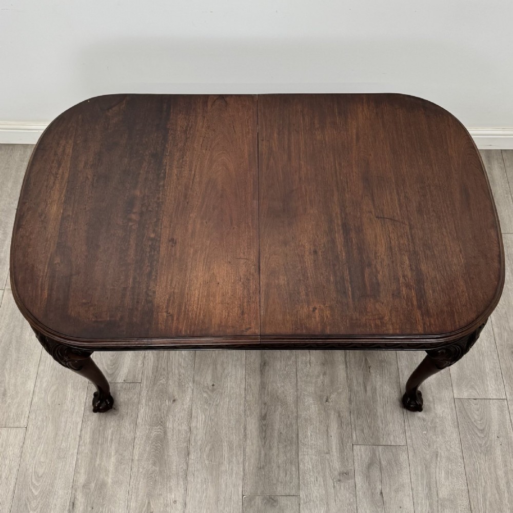 An Edwardian mahogany extending dining table featuring a carved frieze and cabriole legs terminating in ball-and-claw feet. View X
