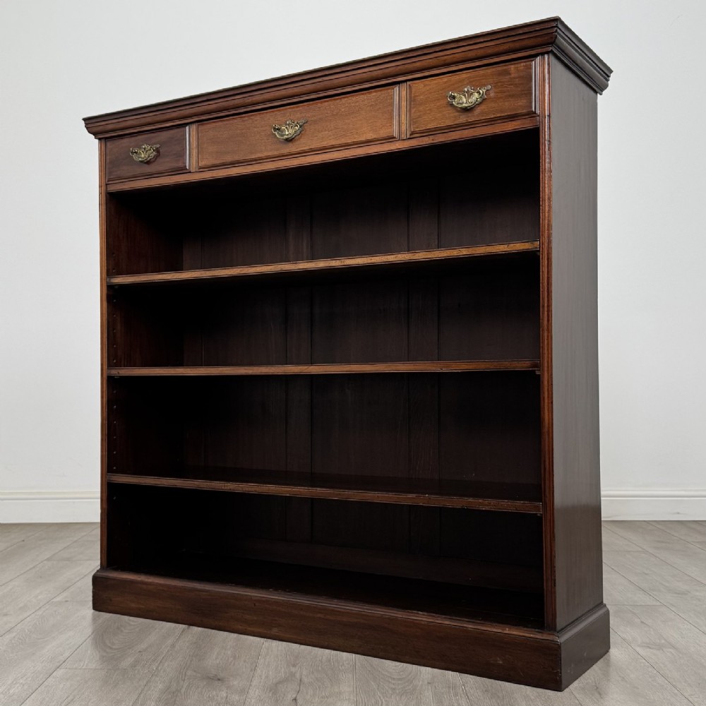 An Edwardian dark mahogany open bookcase featuring three frieze drawers with brass drop handles and three adjustable wooden shelves above a plinth base. View III