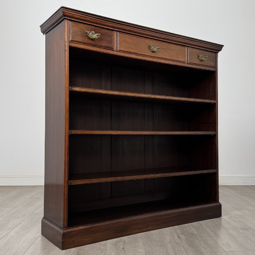 An Edwardian dark mahogany open bookcase featuring three frieze drawers with brass drop handles and three adjustable wooden shelves above a plinth base. View IX