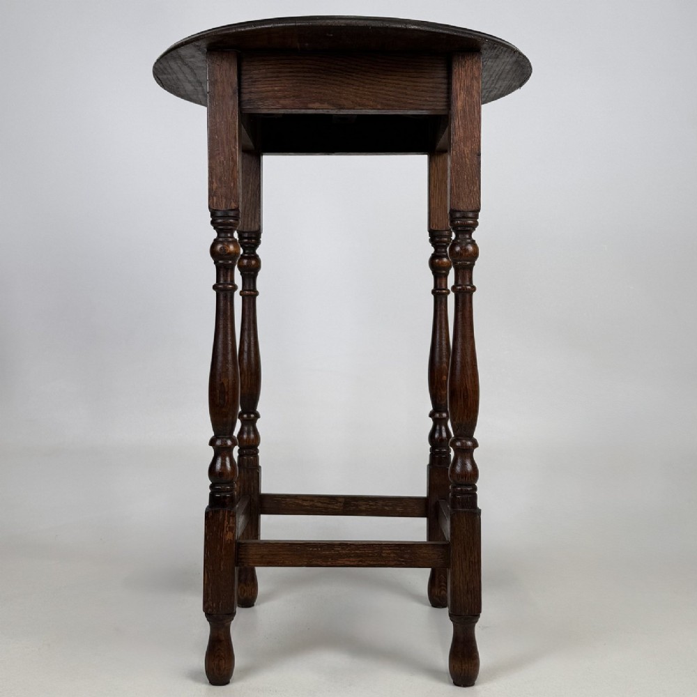 A tall dark oak Jacobean style side table featuring a circular top, four slender turned baluster legs, and low square stretchers. View II