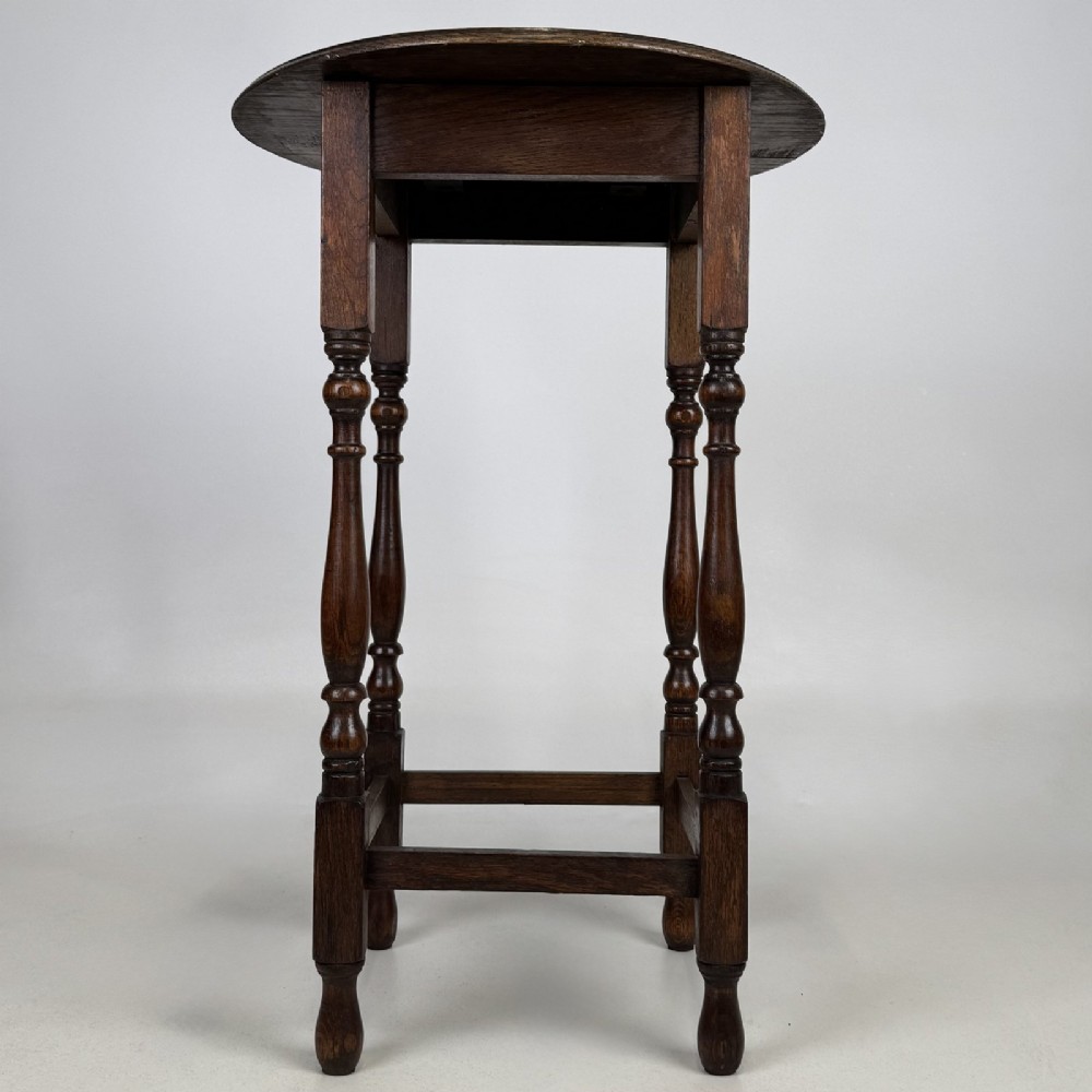 A tall dark oak Jacobean style side table featuring a circular top, four slender turned baluster legs, and low square stretchers. View IV
