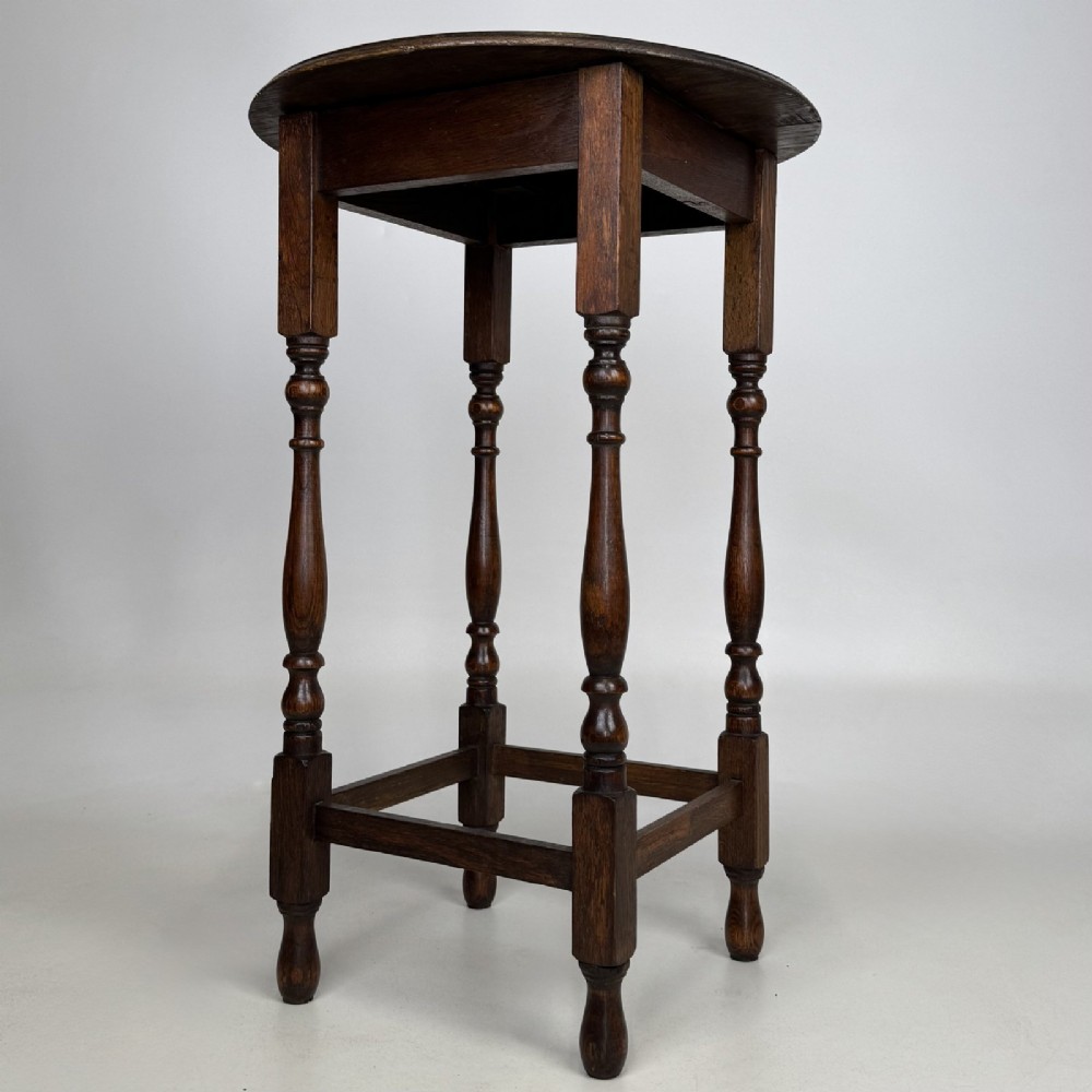 A tall dark oak Jacobean style side table featuring a circular top, four slender turned baluster legs, and low square stretchers. View V
