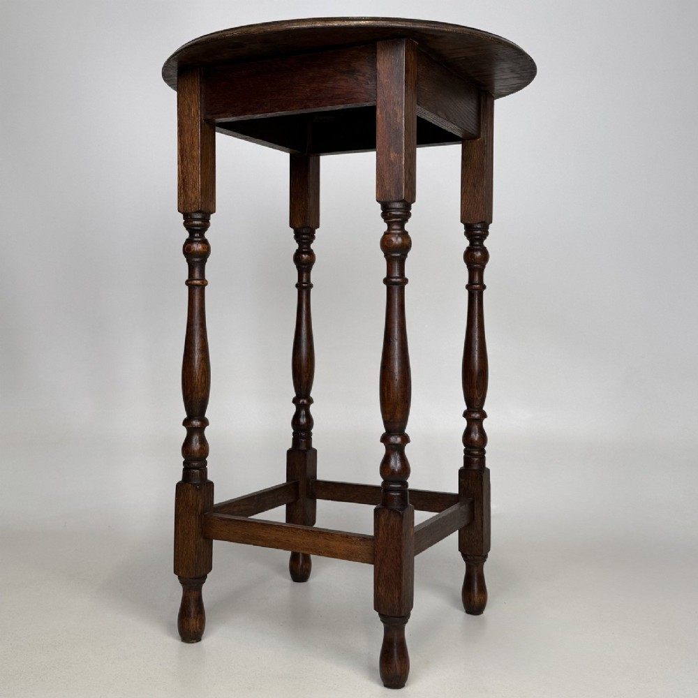 A tall dark oak Jacobean style side table featuring a circular top, four slender turned baluster legs, and low square stretchers. View VI