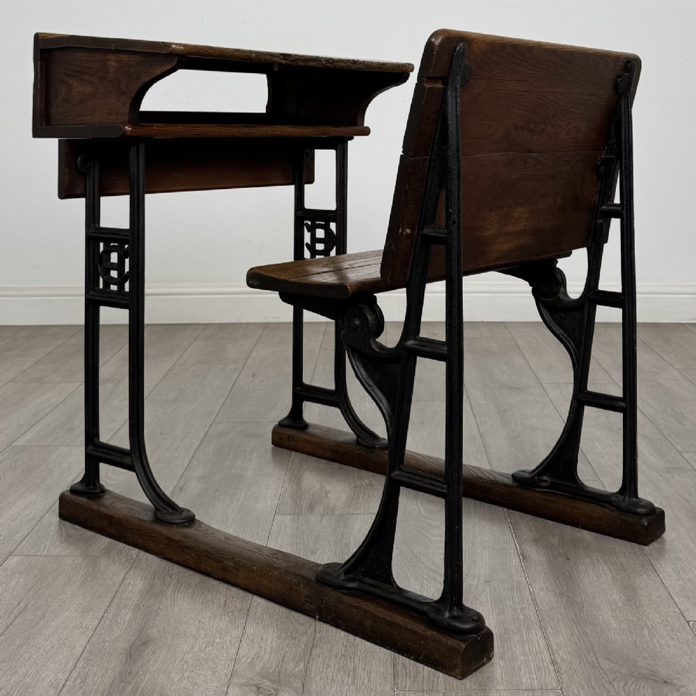 An antique early 20th-century school desk featuring a sloped dark timber top with a storage compartment, attached to a black cast iron frame with an integrated bench seat. View III