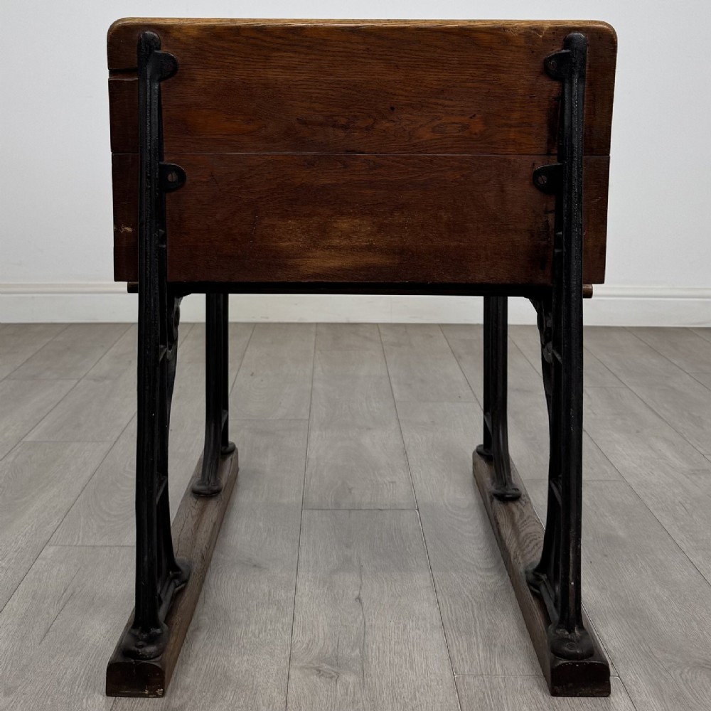 An antique early 20th-century school desk featuring a sloped dark timber top with a storage compartment, attached to a black cast iron frame with an integrated bench seat. View IV