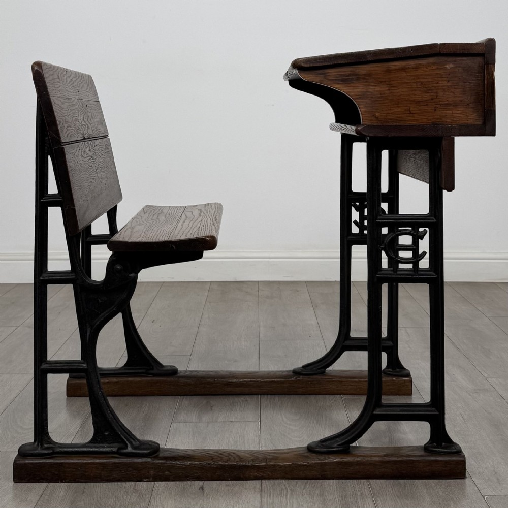 An antique early 20th-century school desk featuring a sloped dark timber top with a storage compartment, attached to a black cast iron frame with an integrated bench seat. View VI