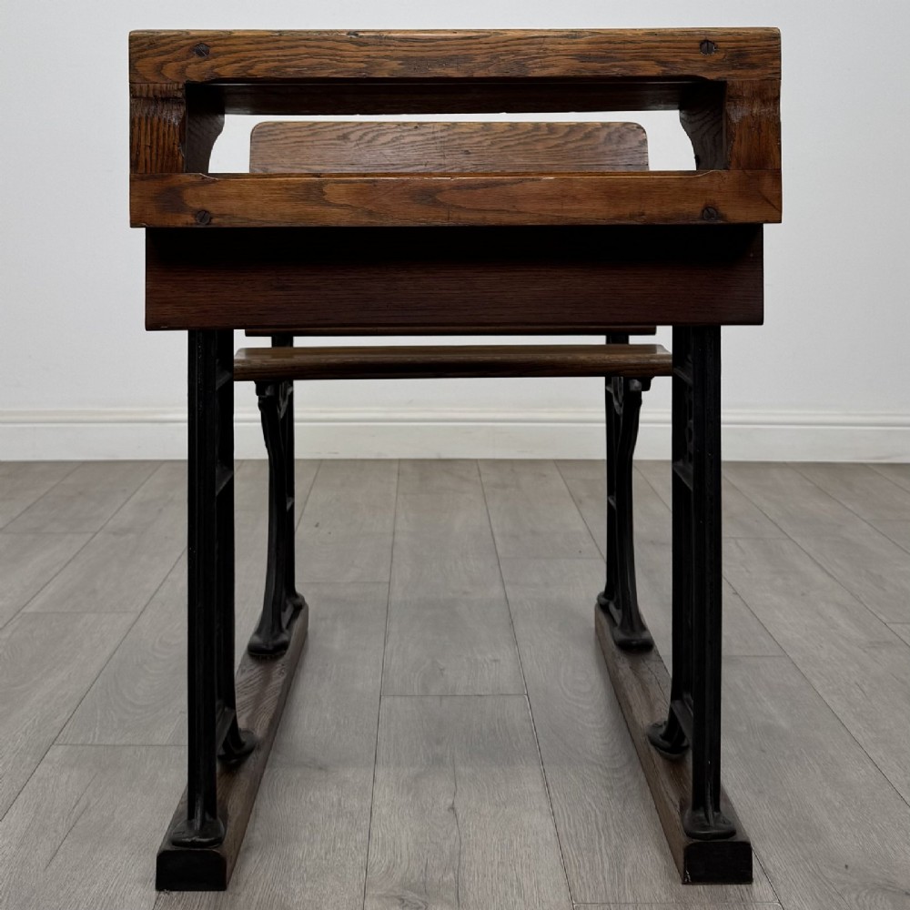 An antique early 20th-century school desk featuring a sloped dark timber top with a storage compartment, attached to a black cast iron frame with an integrated bench seat. View VIII
