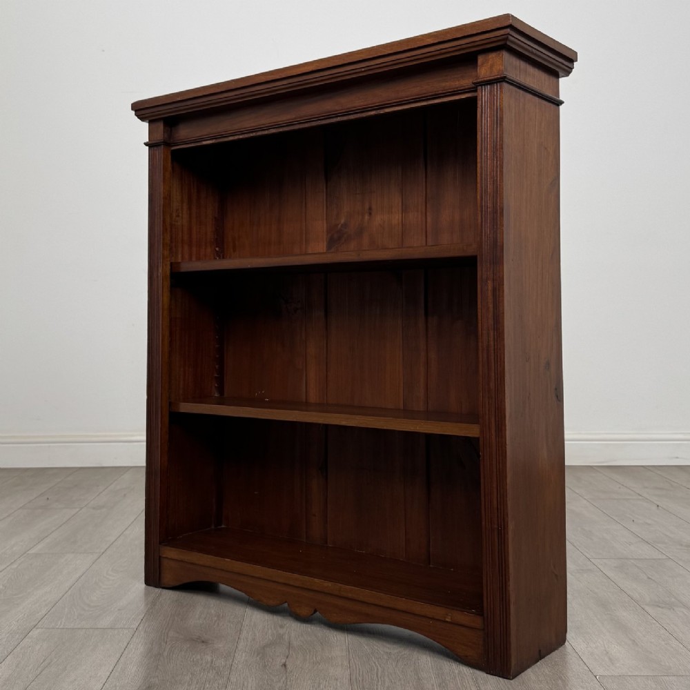 A dark brown Victorian pine open bookcase featuring adjustable shelving, reeded side pilasters, and a shaped apron at the base. View III