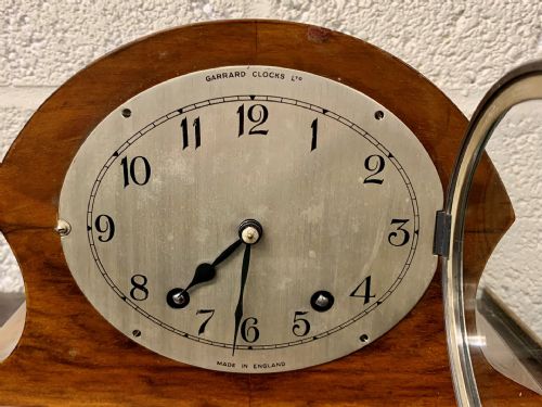 fig 1. An Art Deco Garrard mantel clock featuring a curved walnut case, silvered dial with Arabic numerals, and chrome bezel.