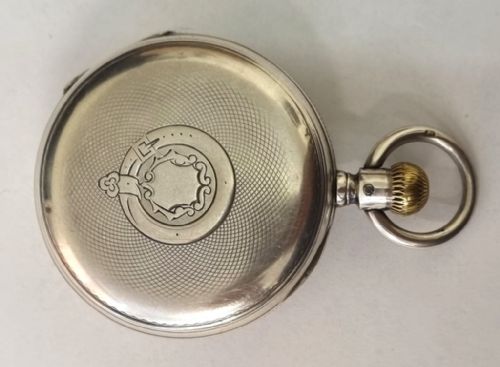 fig 1. A silver half-hunter pocket watch with blue enamel Roman numerals surrounding a central circular glass window revealing dark watch hands.