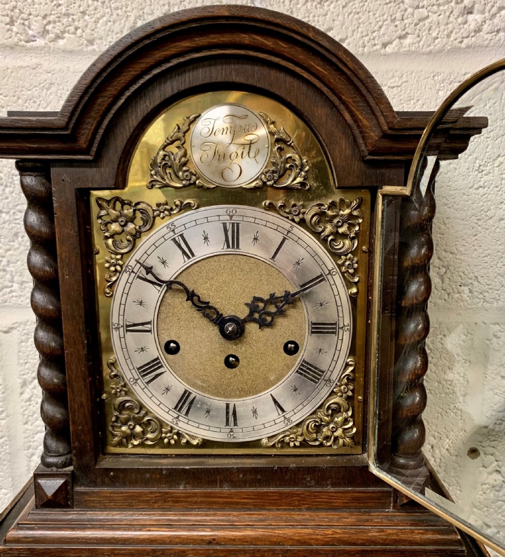 An antique dark oak bracket clock featuring barley twist side columns, a brass dial with a silvered chapter ring, and a Tempus Fugit arch crest.