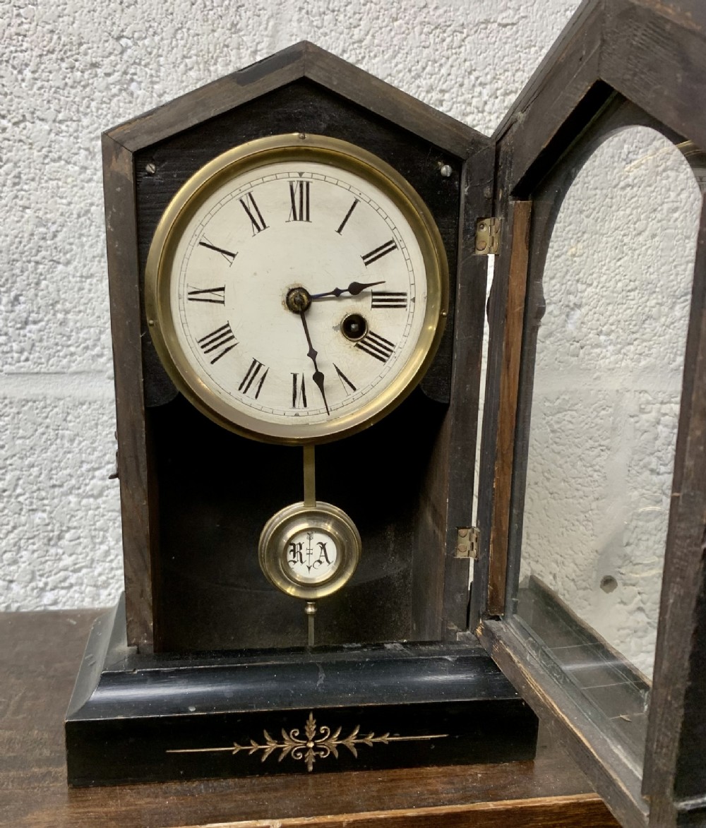 An antique late 19th-century German dark wood mantel clock featuring an arched top case, a brass-rimmed dial with Roman numerals, a visible pendulum, and an open glazed door.