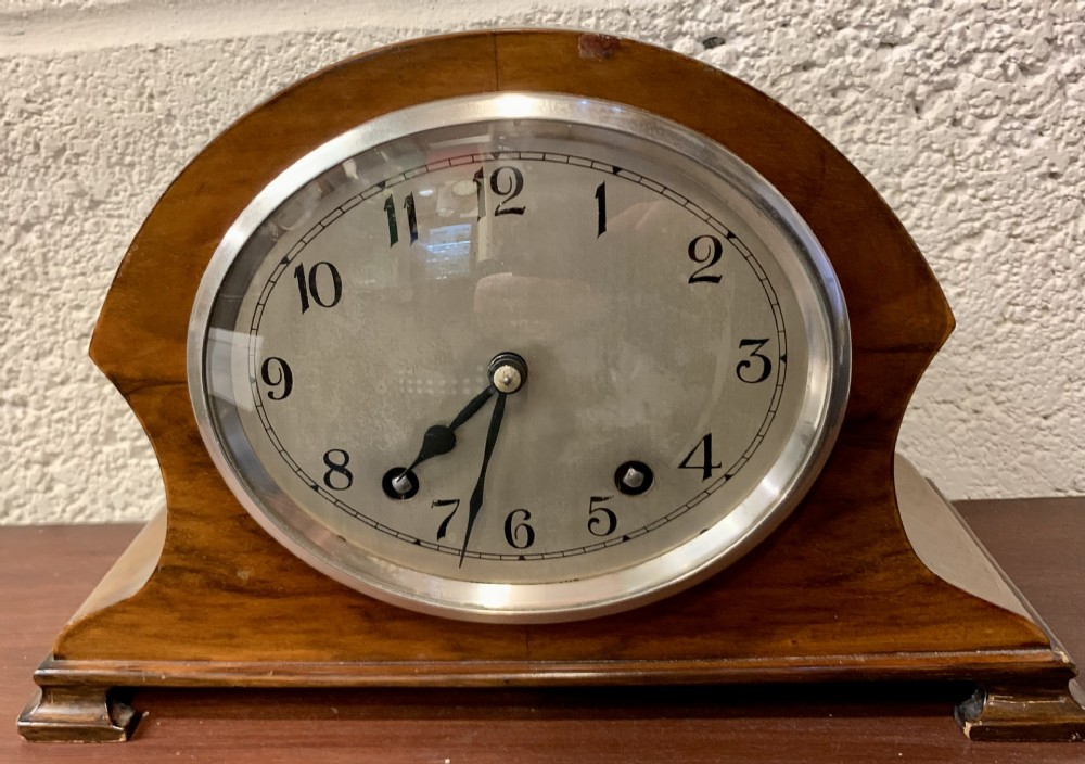 An Art Deco Garrard mantel clock featuring a curved walnut case, silvered dial with Arabic numerals, and chrome bezel.