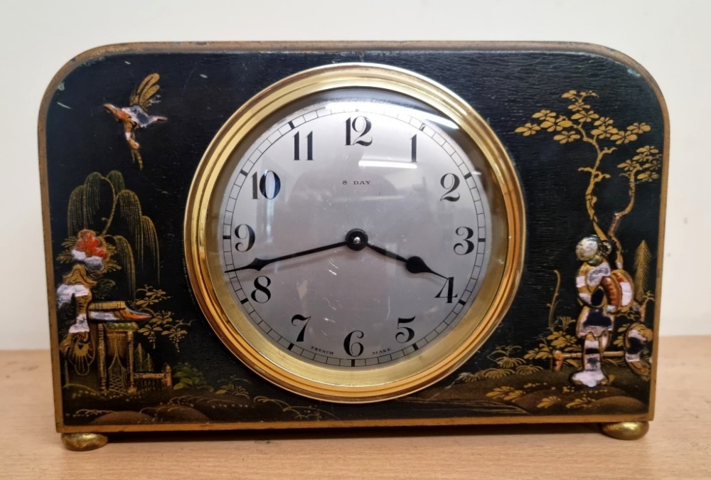 A rectangular black lacquered French mantel clock featuring gold chinoiserie decoration, a brass bezel, and a white dial displaying Arabic numerals.