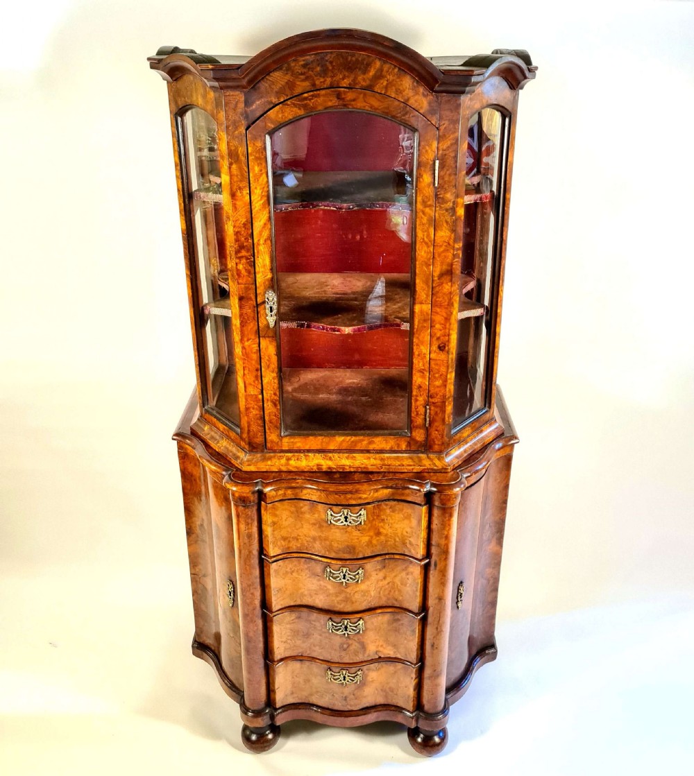 An 18th-century Dutch burr walnut display cabinet featuring a glazed upper section with an arched top above a serpentine base with four drawers.