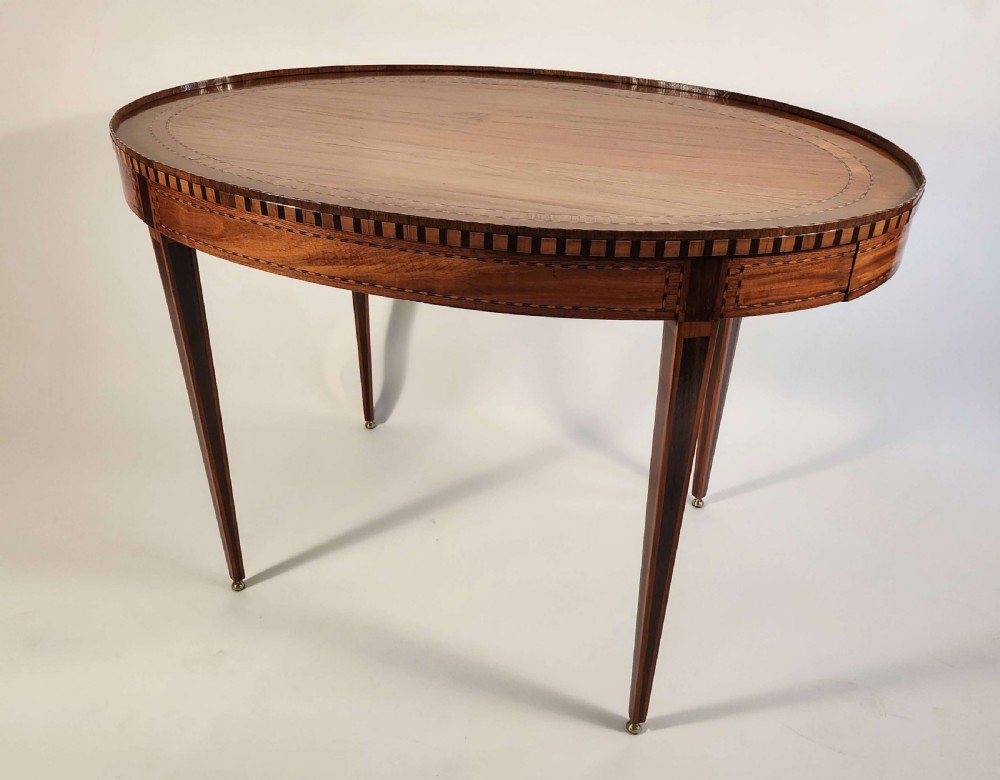 An 18th-century Dutch oval satinwood side table with inlaid geometric banding around the rim and apron, supported by four tapered square legs with brass feet.