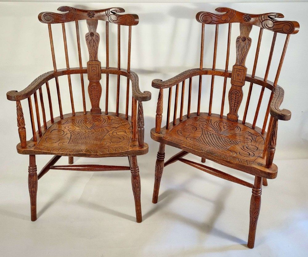 A pair of 19th-century carved oak Windsor armchairs featuring spindle backrests, carved crest rails, and relief basket motifs carved into the seats.