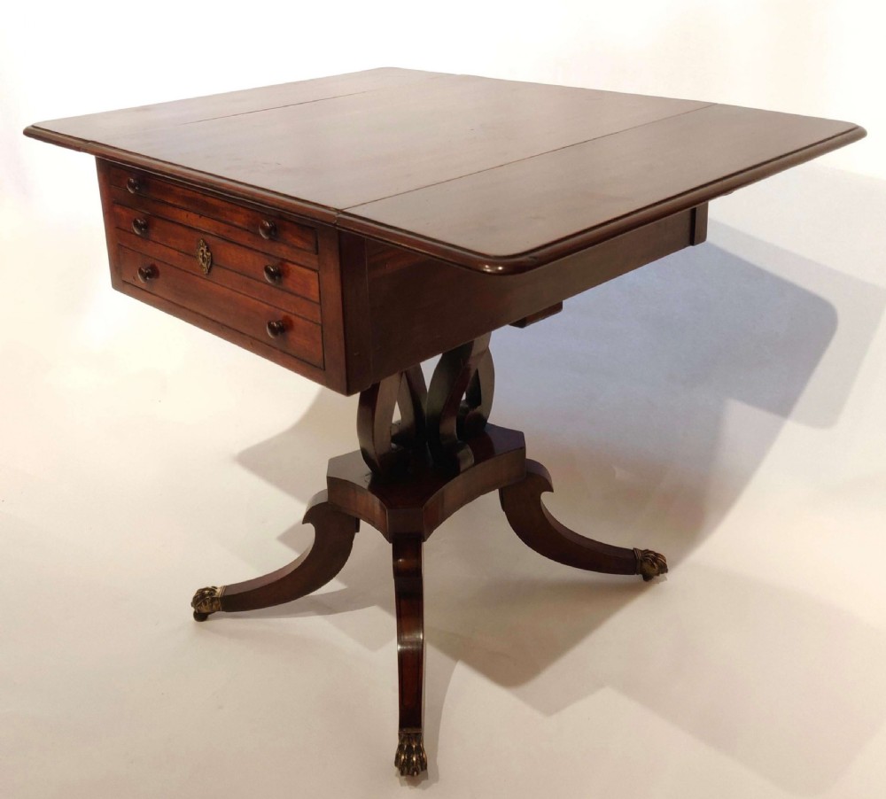 A Regency mahogany drop flap table featuring two drawers, a central carved pedestal, and four splayed legs with brass lion paw castors. View II