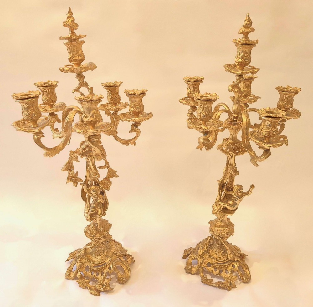 A pair of ornate French ormolu multi-arm candelabra featuring sculpted putti figures and intricate scrolling acanthus leaf bases.