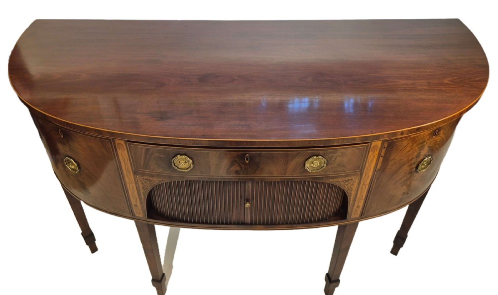 A George III mahogany bow-fronted sideboard featuring flame mahogany drawer fronts, boxwood inlay, and tapered square legs. View II