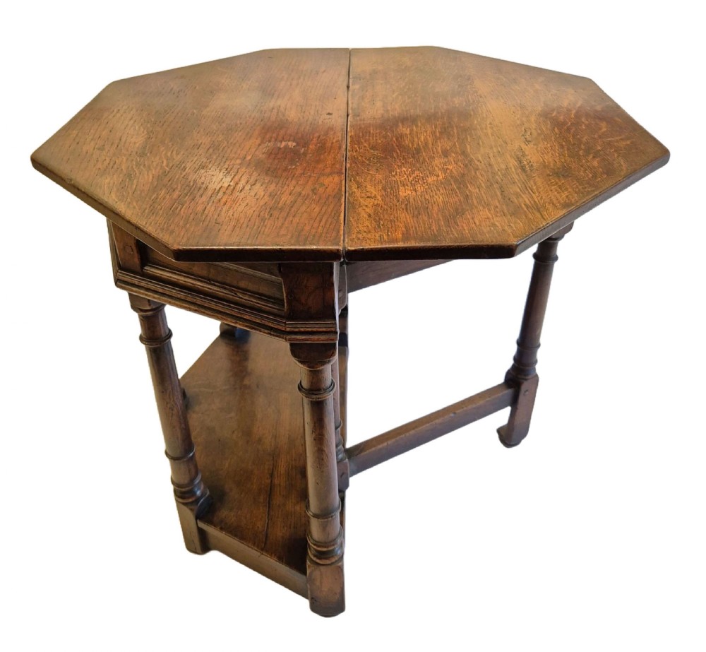 A dark oak credence side table featuring a canted top, turned column legs, a lower shelf, and a fold-over leaf mechanism. View II