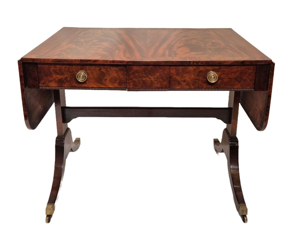 A Regency mahogany sofa table with flame mahogany veneers, twin drop leaves, two frieze drawers with brass handles, and sweeping legs on brass castors. View II