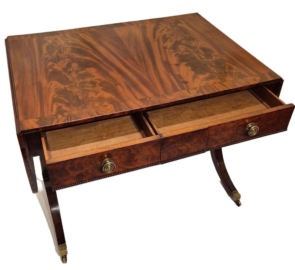 A Regency mahogany sofa table with flame mahogany veneers, twin drop leaves, two frieze drawers with brass handles, and sweeping legs on brass castors. View III