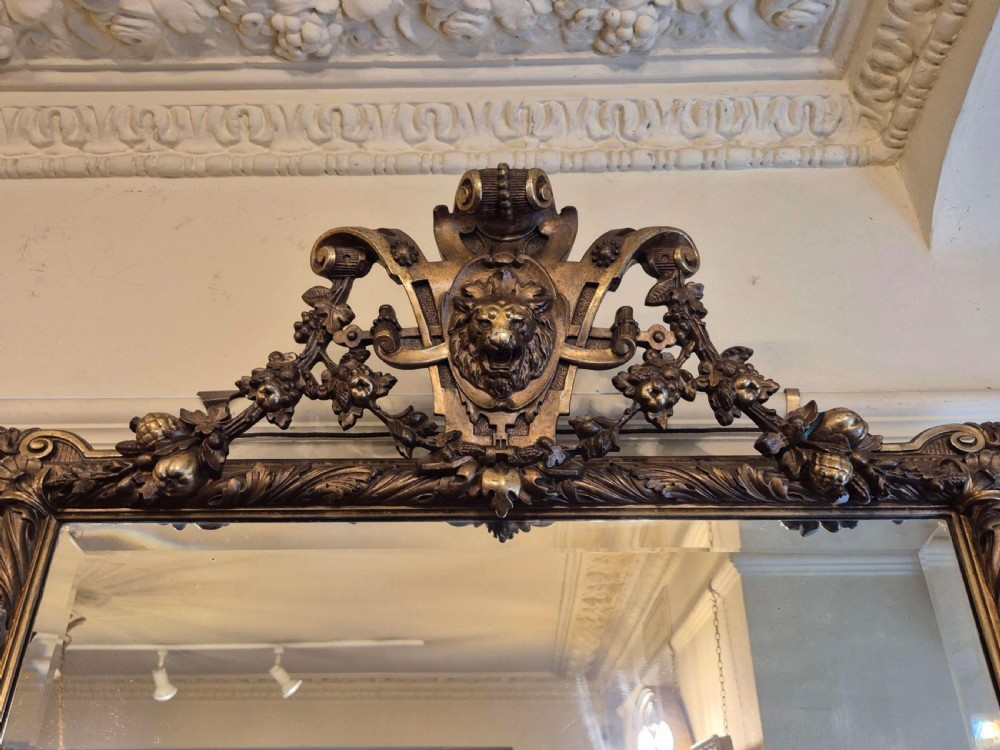 A rectangular giltwood and gesso wall mirror featuring an ornate pediment sculpted with a lion head mask and acanthus leaf details. View II