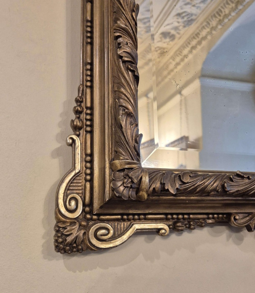 A rectangular giltwood and gesso wall mirror featuring an ornate pediment sculpted with a lion head mask and acanthus leaf details. View III