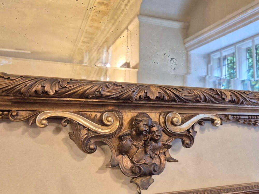 A rectangular giltwood and gesso wall mirror featuring an ornate pediment sculpted with a lion head mask and acanthus leaf details. View IV