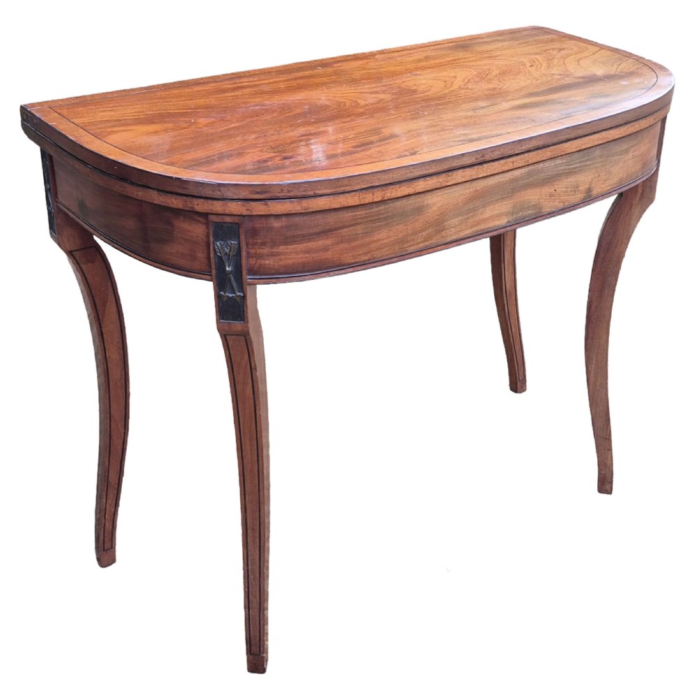 An antique George III mahogany demilune card table featuring slender shaped legs, inlaid stringing, and a fold-over top.