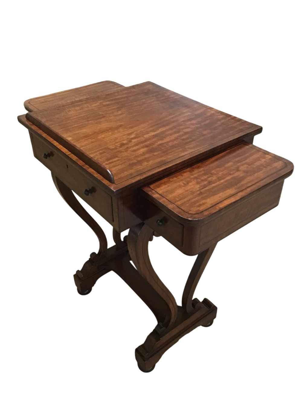 An antique Regency mahogany sofa table featuring two extending side slides, ebony stringing details, drawer knobs, and curved pedestal legs on castors.