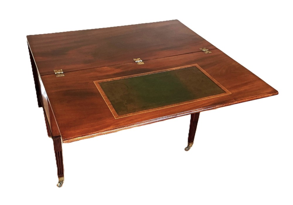 An antique George III mahogany library table featuring an arched central aperture, multiple drawers with dark turned knobs, and reeded tapered legs on brass castors. View III